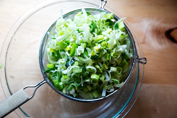 Leeks in a sieve over a large glass bowl.