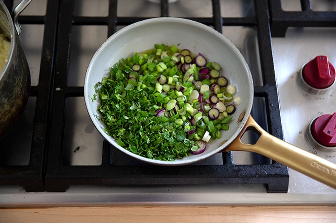 A small skillet on the stovetop with scallions and cilantro in it.