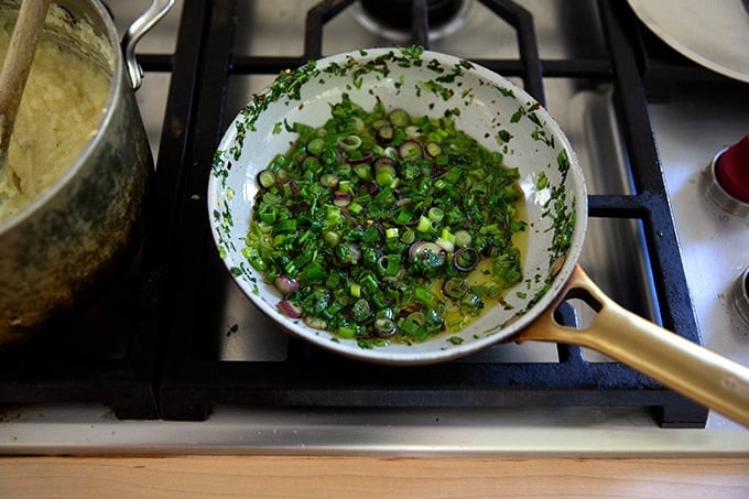 Cooked scallions and cilantro in a small skillet stovetop.