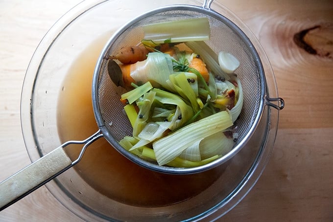 A sieve holding cooked vegetables set over a bowl of homemade vegetable stock.