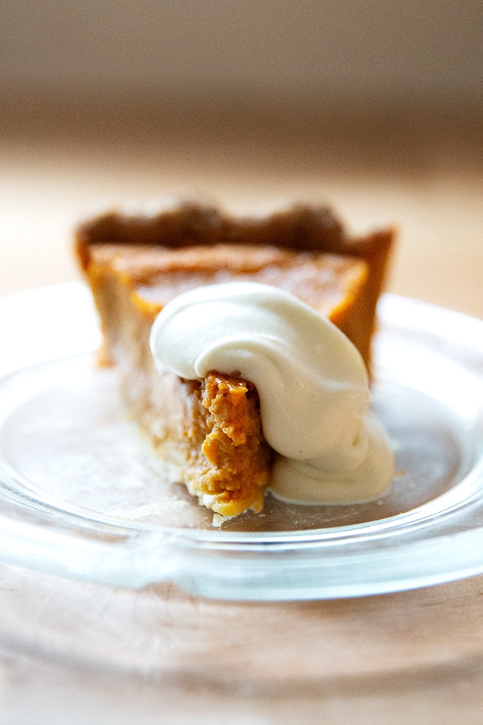 A slice of pumpkin pie on a plate with a dollop of whipped cream on top.
