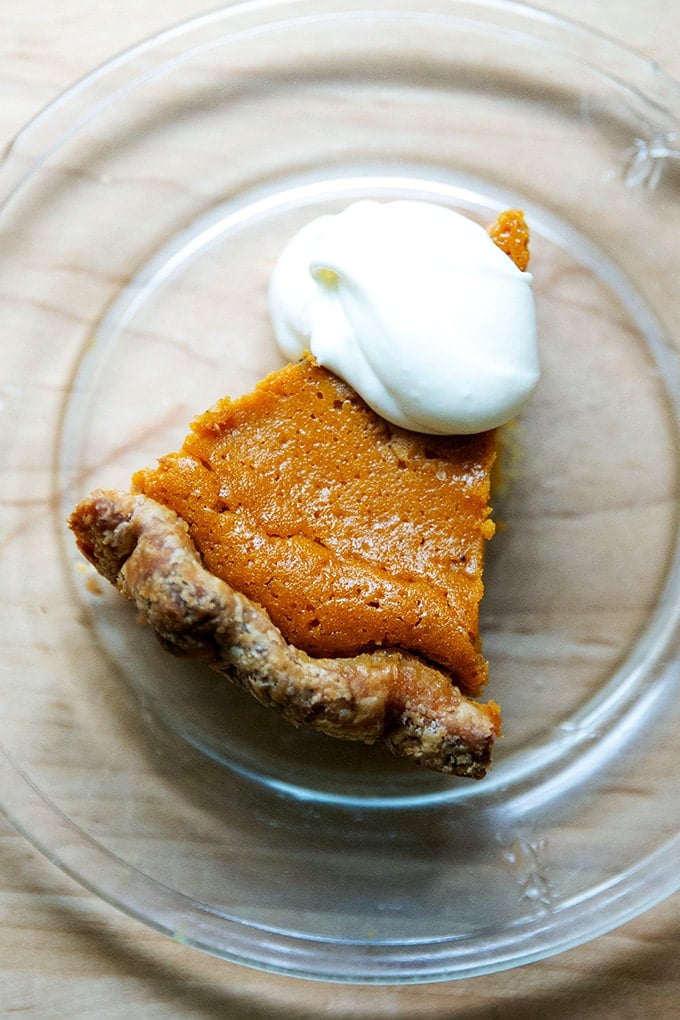 A slice of pumpkin pie on a plate with a dollop of whipped cream on top.