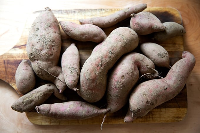 A pile of sweet potatoes on a cutting board.