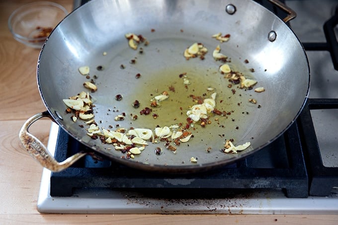 A large skillet stovetop with some olive oil, slice garlic, and crushed red pepper flakes inside. 