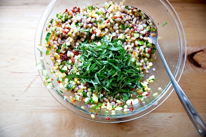 Basil added to a bean salad in a large bowl.