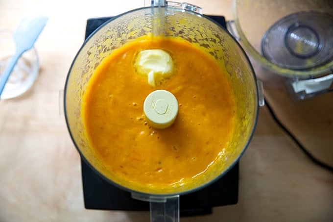 A food processor filled with roasted yellow tomato sauce and a knob of butter.