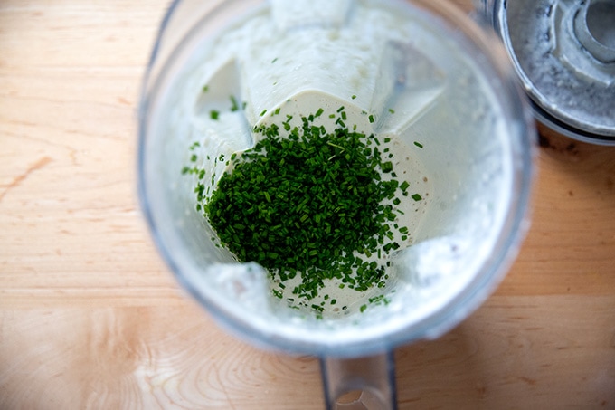 Chives added to a Vitamix filled with blended vegan ranch dressing.