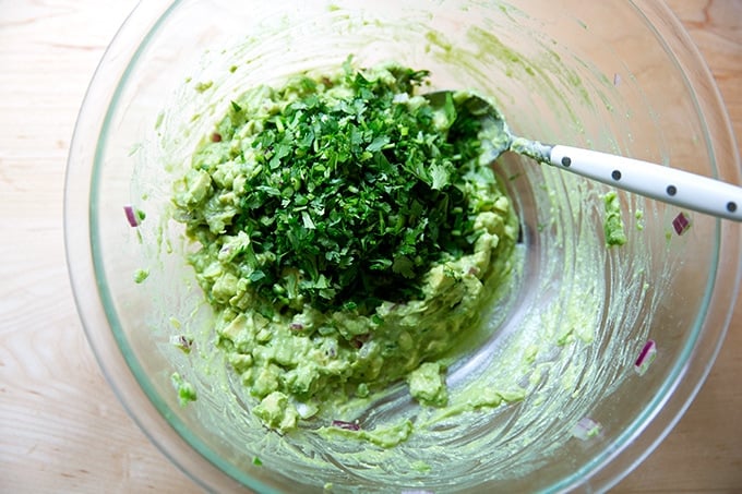 A large bowl of just-made guacamole with cilantro added.