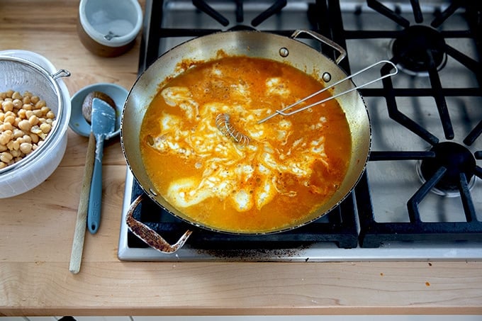 A skillet on the stovetop holding the makings of curried Thai chickpeas.