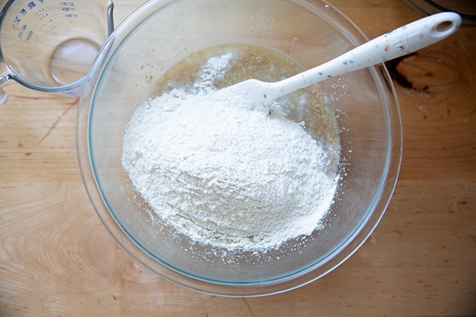 Adding the flour to a bowl of water, oats, maple syrup, yeast, and water.