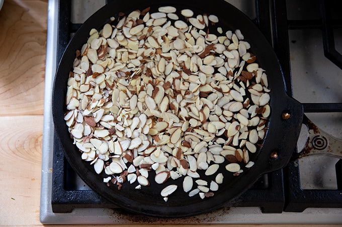 A skillet holding almonds on the stovetop slowly toasting.