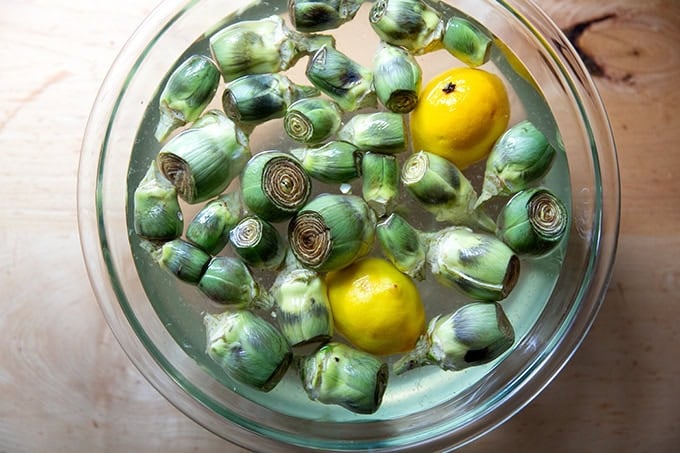 A large bowl filled with water, lemon, and baby artichokes cleaned and trimmed. - 3