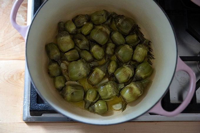 A large pot on the stovetop filled with baby artichokes halfway through their cooking process. - 6