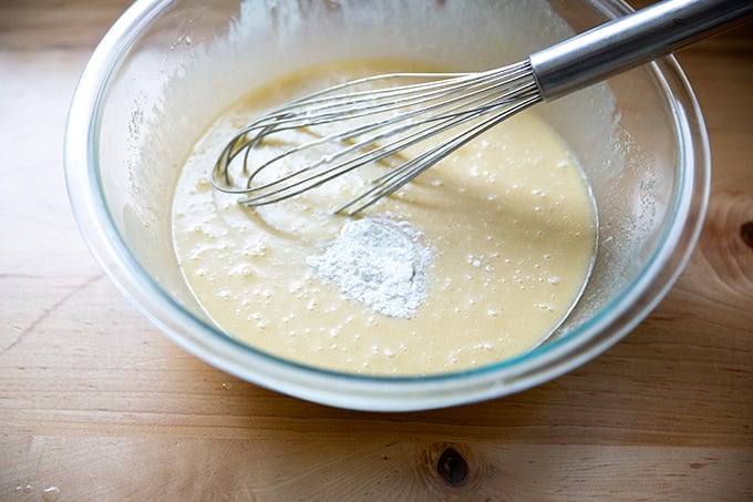 A large bowl filled with wet ingredients to make pound cake plus baking powder.