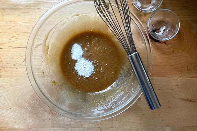 A bowl of white chocolate-madacamia nut cookie batter in the making with a whisk on top.