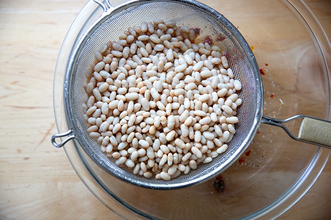 White beans in a strainer set over a bowl.