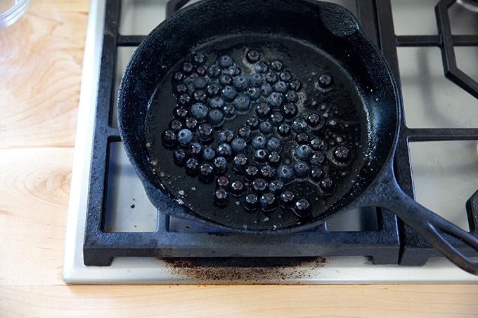 A cast iron skillet on the stovetop with blueberries and melted butter in it.