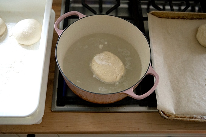 A pretzel roll floating in a pot of boiling water.