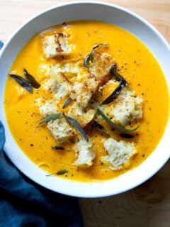 A bowl of roasted butternut squash soup topped with croutons and fried sage.
