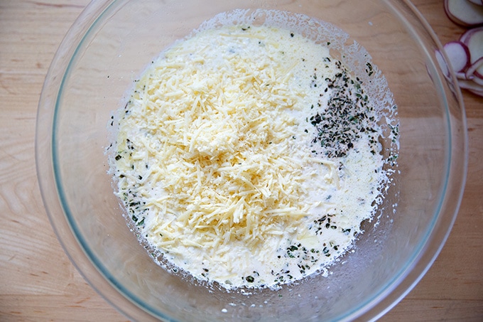 A large bowl filled with heavy cream, grated cheese, thyme, and chicken stock.