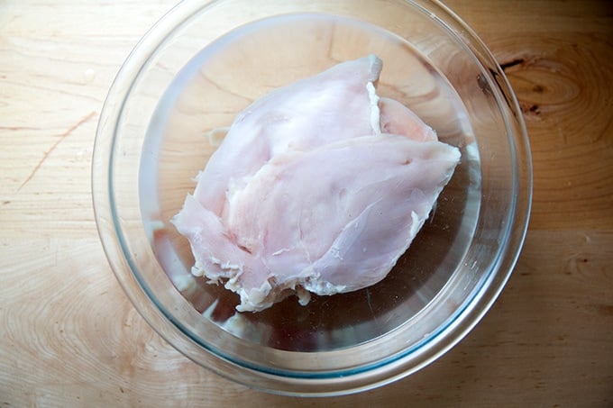Brined chicken breasts in a large glass bowl.