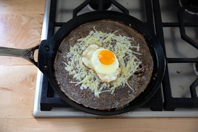 An egg-and-gruyere filled buckwheat crepe in the process of being made in a skillet on the stovetop.