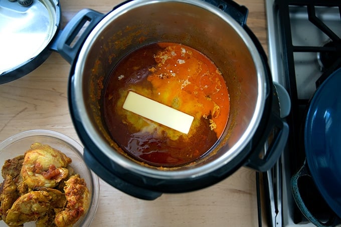 A stick of butter added to an Instant Pot filled with butter chicken sauce.