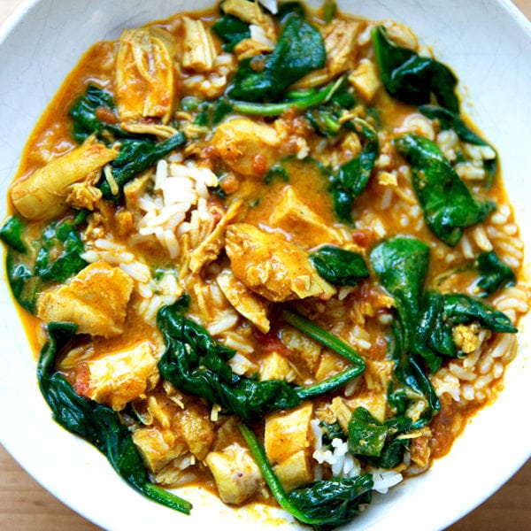 A bowl of butter chicken with spinach and rice.