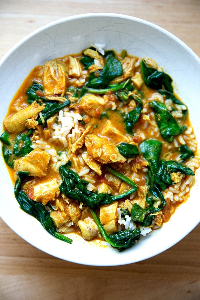 A bowl of butter chicken with spinach and rice.