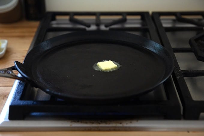A nonstick crepe pan on a stovetop with a teaspoon of butter in the center.