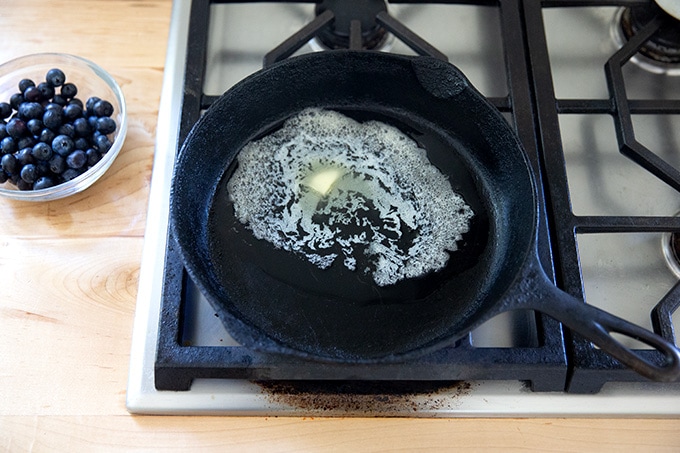 A cast iron skillet on the stovetop with butter melted in it.
