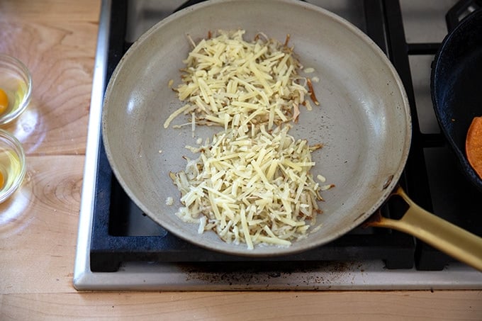 A skillet with two piles of potatoes crisping with cheese on top.