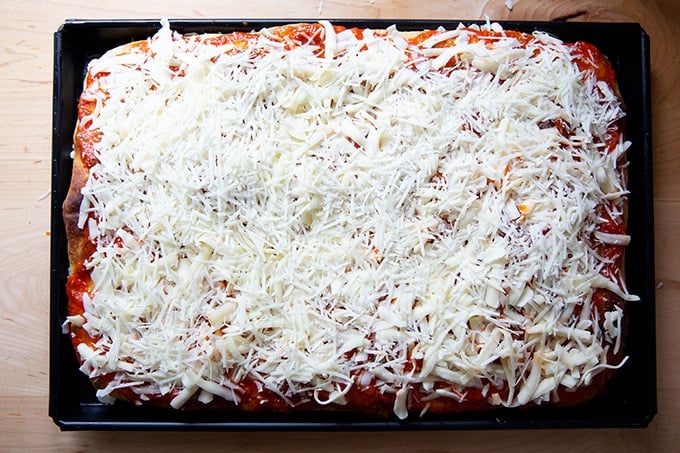 A Sicilian-style pizza crust topped with sauce and cheese.