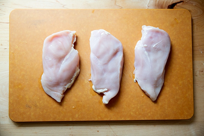 Three chicken breasts on a cutting board.