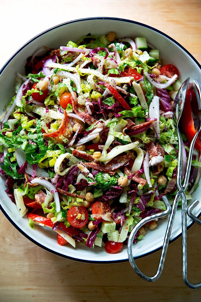 A classic chopped salad in a large salad bowl with tongs.