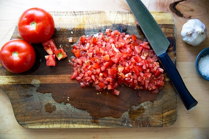A cutting board with chopped tomatoes on top.