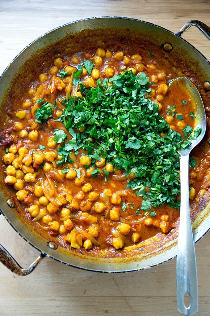 A skillet on the stovetop holding just cooked curried Thai chickpeas with cilantro just added.