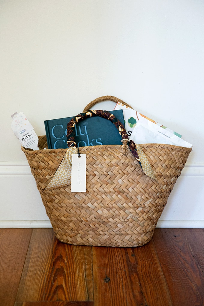 A straw bag holding a cookbook, spatula, flour and other gifts for mother's day.