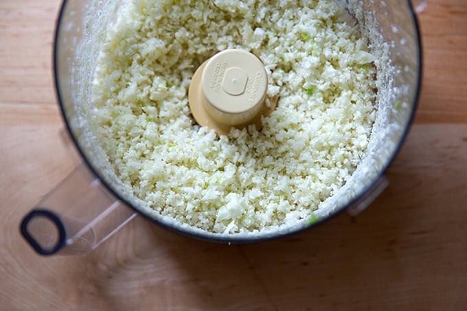 A food processor filled with finely chopped cauliflower.