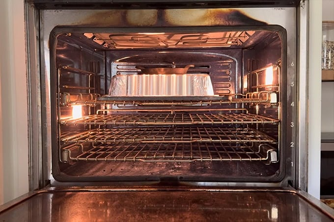 A disposable foil pan turned over a baguette on a baking steel in a oven.