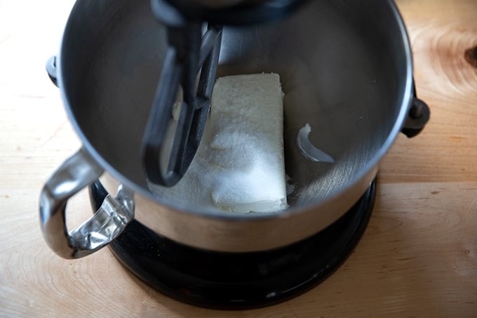 A bowl of cream cheese and sugar attached to a stand mixer.