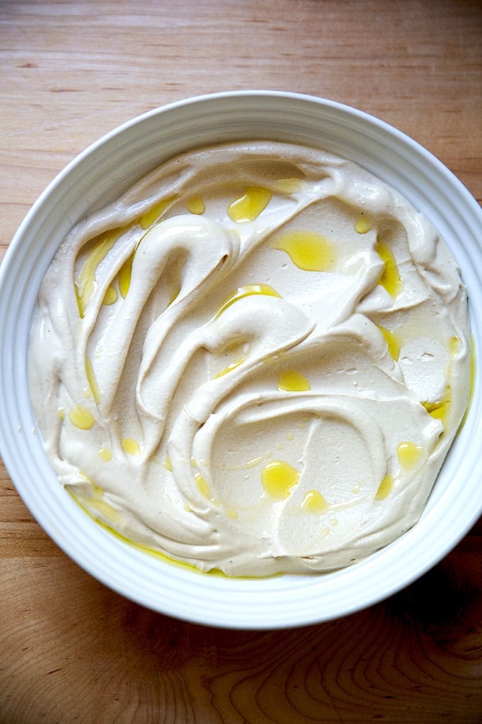 A bowl of creamy hummus drizzled with olive oil on a plate.