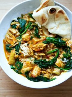 A bowl of butter chicken with spinach, rice and naan.