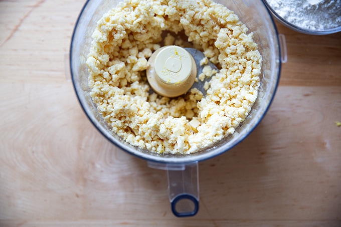 A food processor filled with the ingredients to make lemon-almond snowball cookie dough, partly blended. 