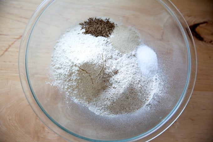 A bowl of bread flour, rye flour, caraway seeds, yeast, and salt.