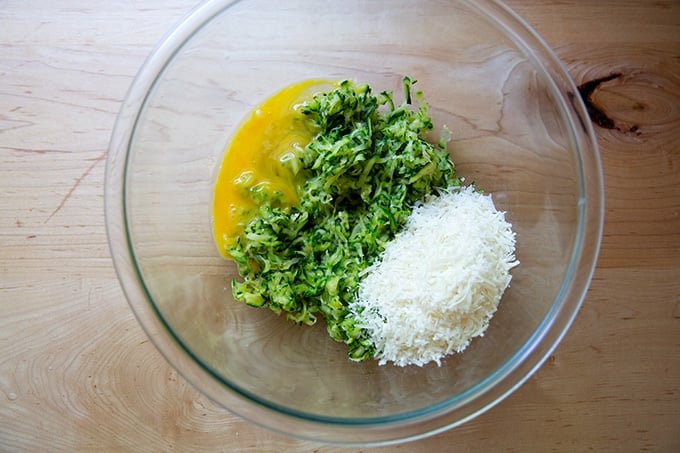 A large bowl filled with a beaten egg, grated zucchini, and grated parmesan.