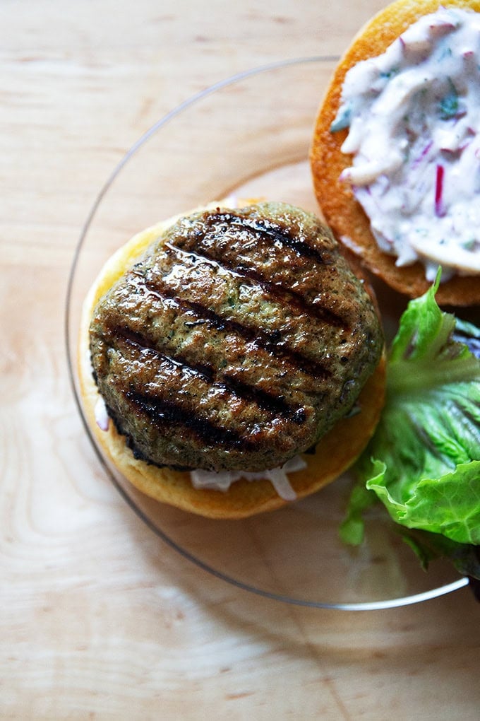 A plated turkey burger aside some lettuce, bun spread with raita.