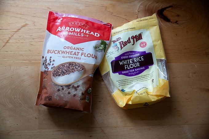 A bag of buckwheat flour aside a bag of white rice flour on a countertop.