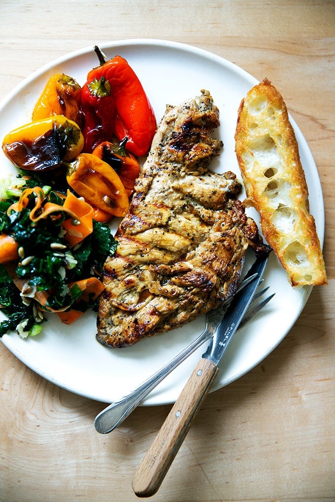 Grilled chicken breast on a plate aside bread, peppers, and salad.