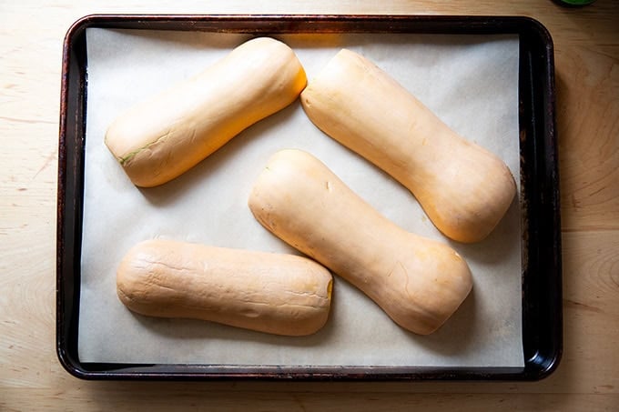 Halved butternut squash unbaked on a parchment-lined sheet pan. - 4